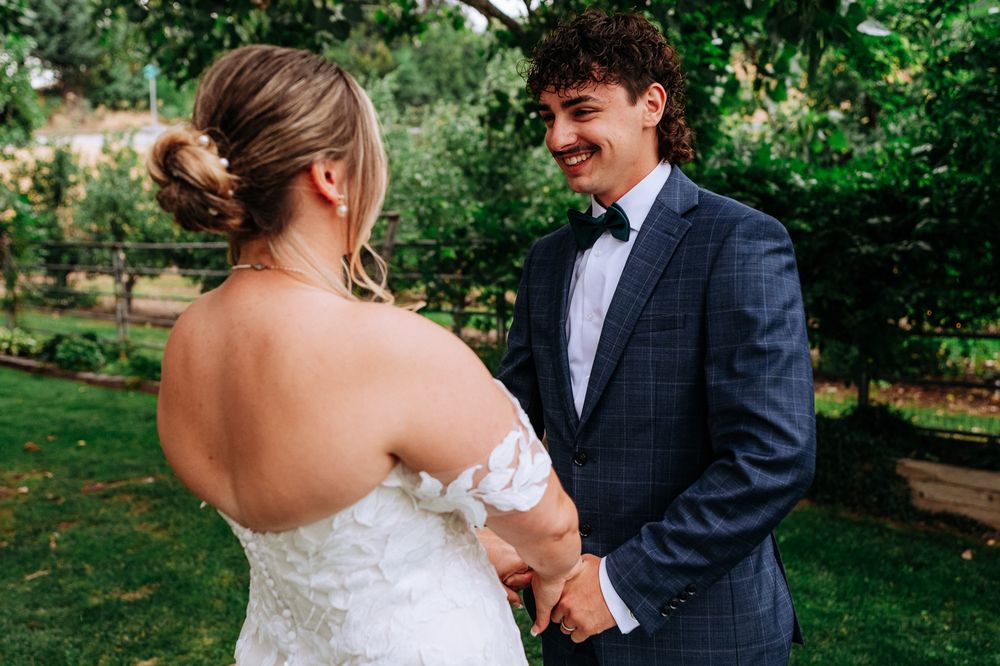 Bride and groom holding hands outdoors, groom smiling in navy suit, bride in white lace dress at garden wedding.