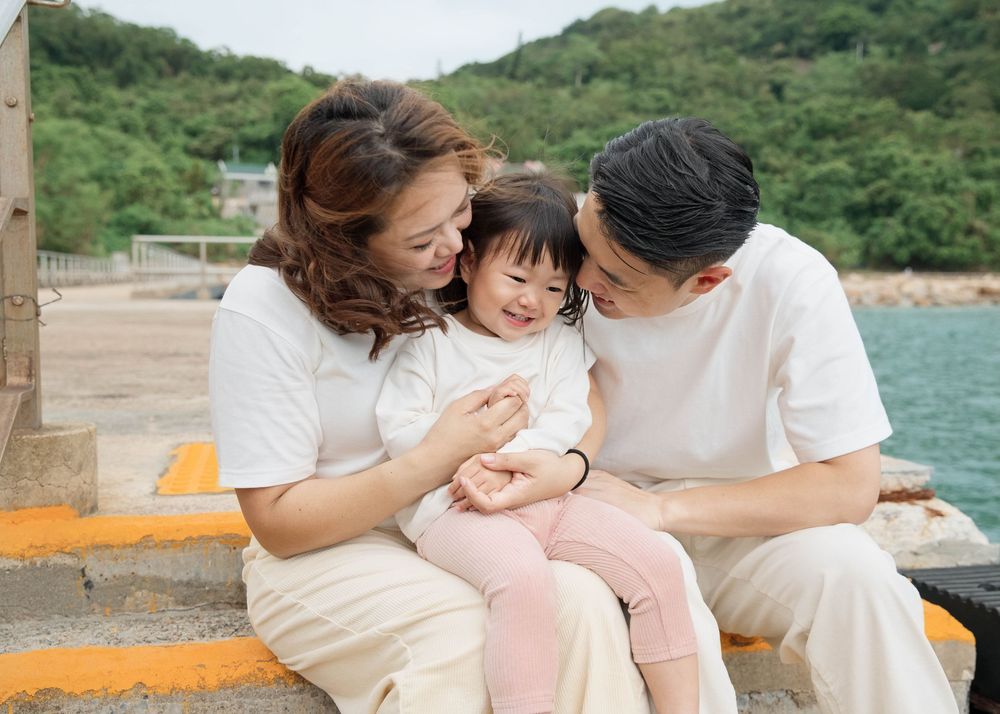 A mother and father smiling and cuddling their 2-year-old daughter during a relaxed outdoor family portrait session in Clear Water Bay
