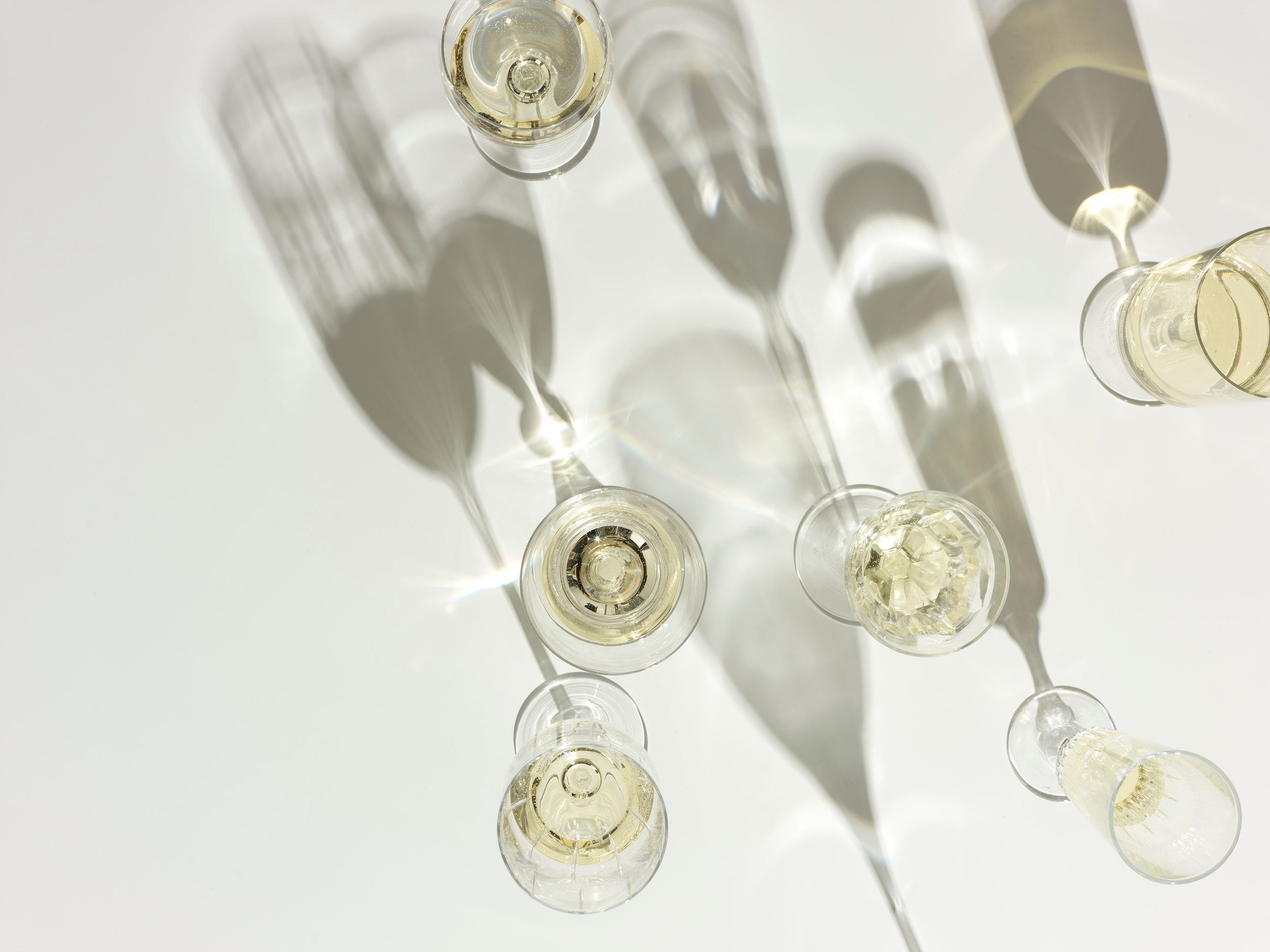 Overhead view of elegant champagne flutes casting long shadows on a white surface at a celebration.