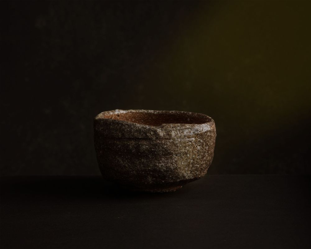 Rustic handmade dark ceramic tea bowl with rough textured surface on a dark background.