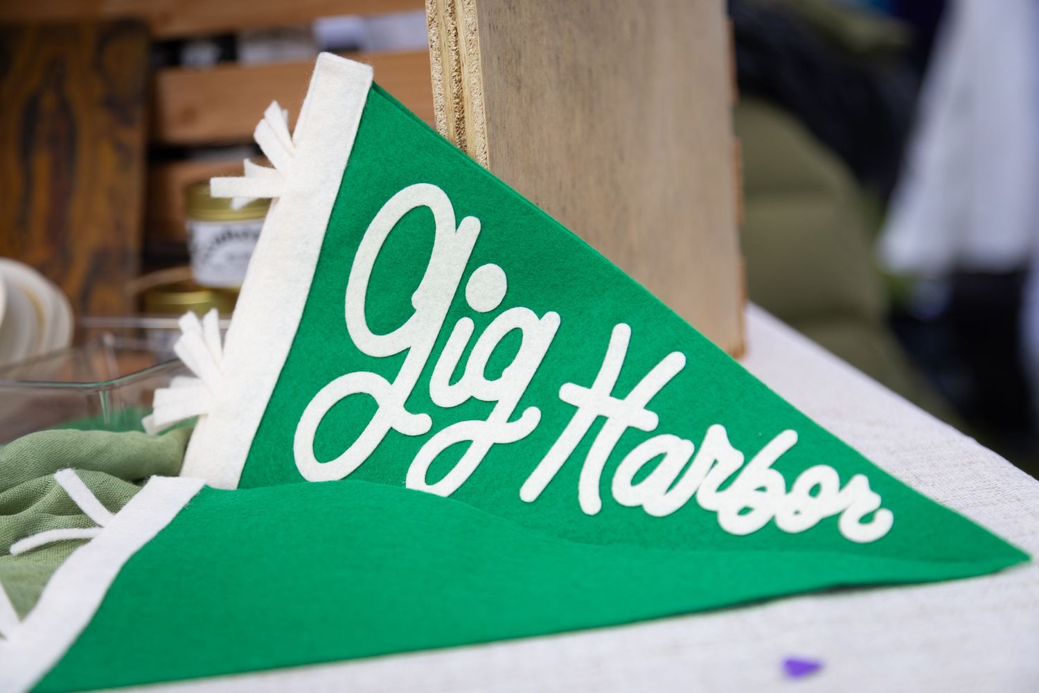 Green felt pennant flag with white cursive text reading Gig Harbor displayed on a white wooden surface.