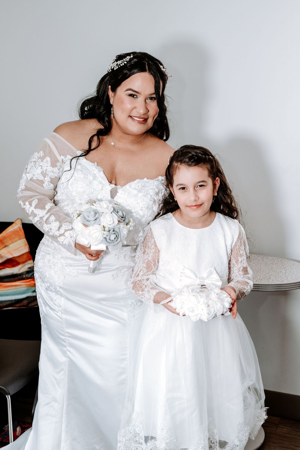 Bride in lace wedding gown holds bouquet beside flower girl in white dress with ring pillow.