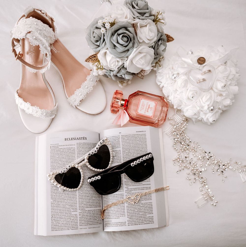 Elegant bridal flat lay with lace heels, pearl sunglasses, floral bouquet, perfume, and accessories.