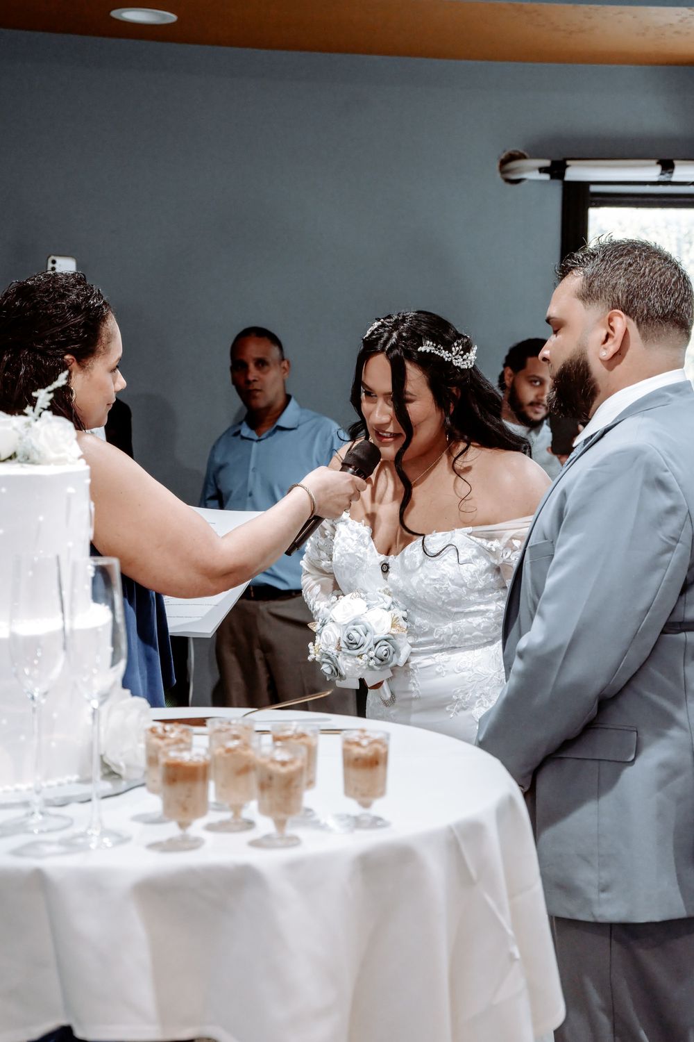 Bride and groom cutting wedding cake at reception with guests watching in background.