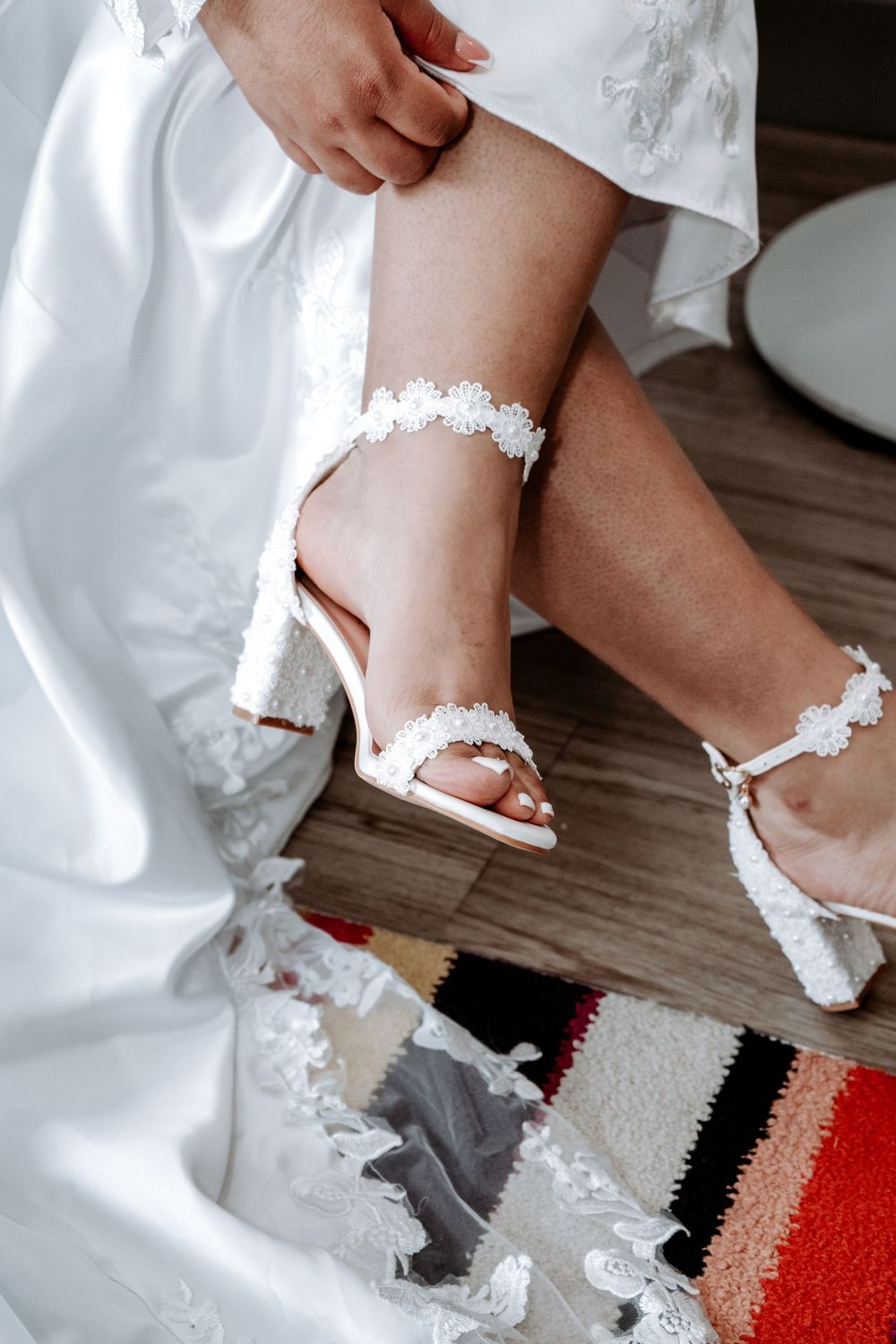 Bride putting on white lace heeled sandals with matching garter on wedding day.