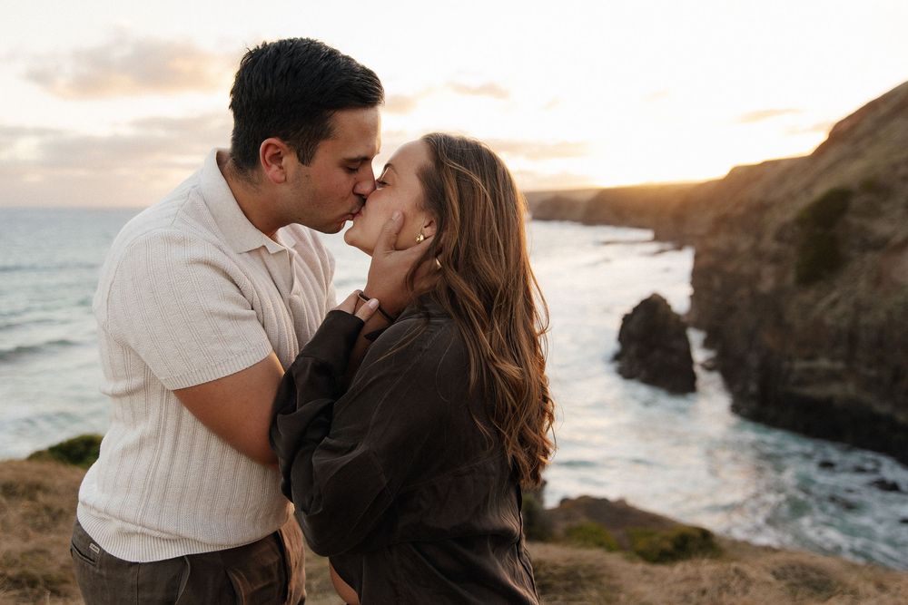 Romantic couple sharing a kiss on rocky coastal cliffs at sunset.