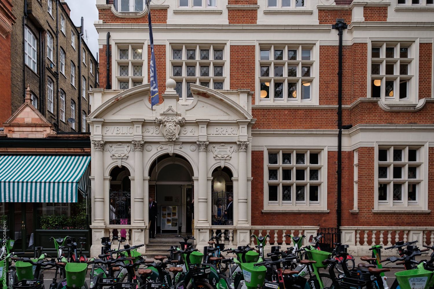 Historic red brick building with white stone entrance and green rental bikes parked in front on a London street.