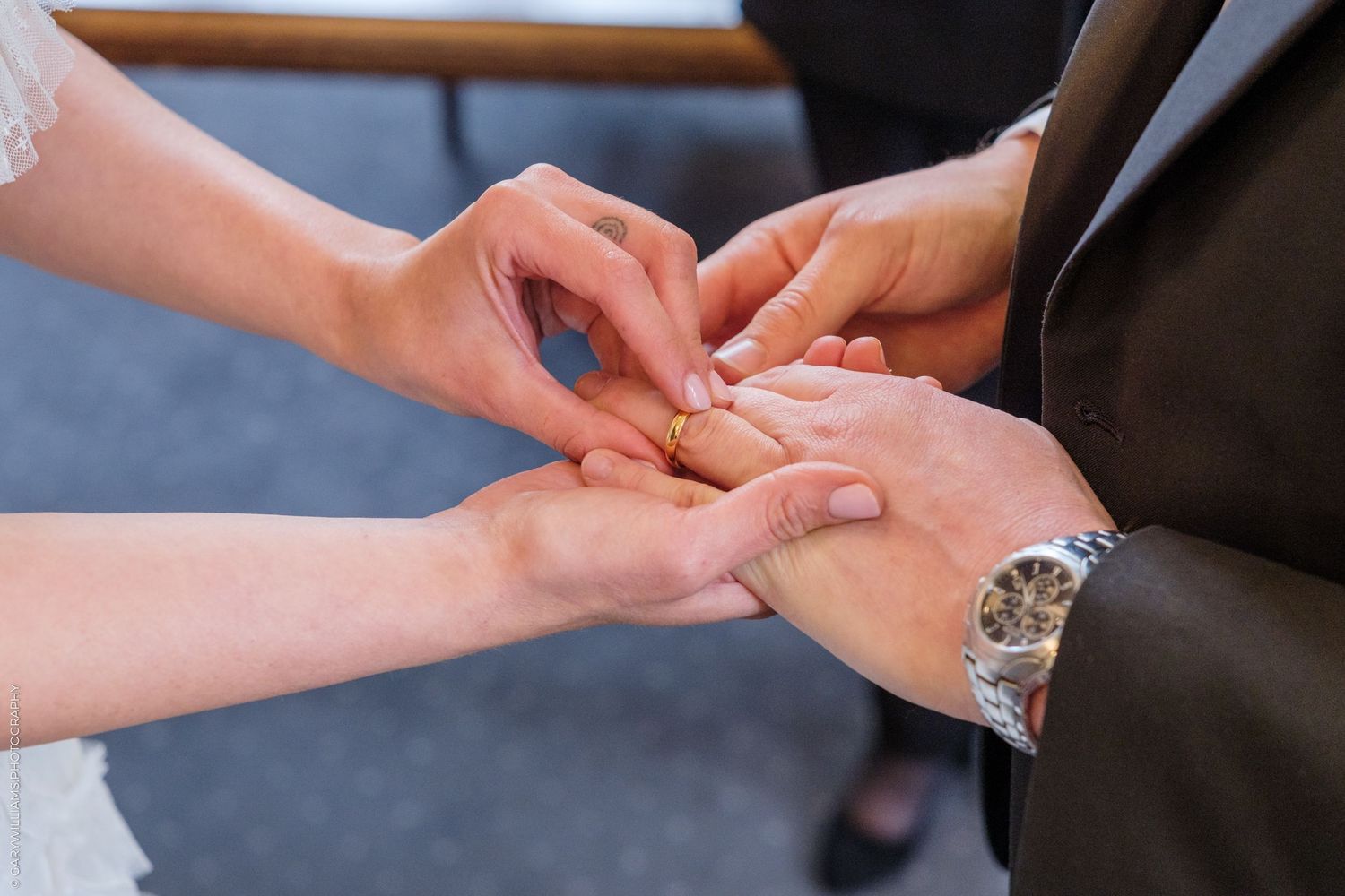 Close-up of a bride placing a gold wedding ring on the groom's finger during a wedding ceremony.