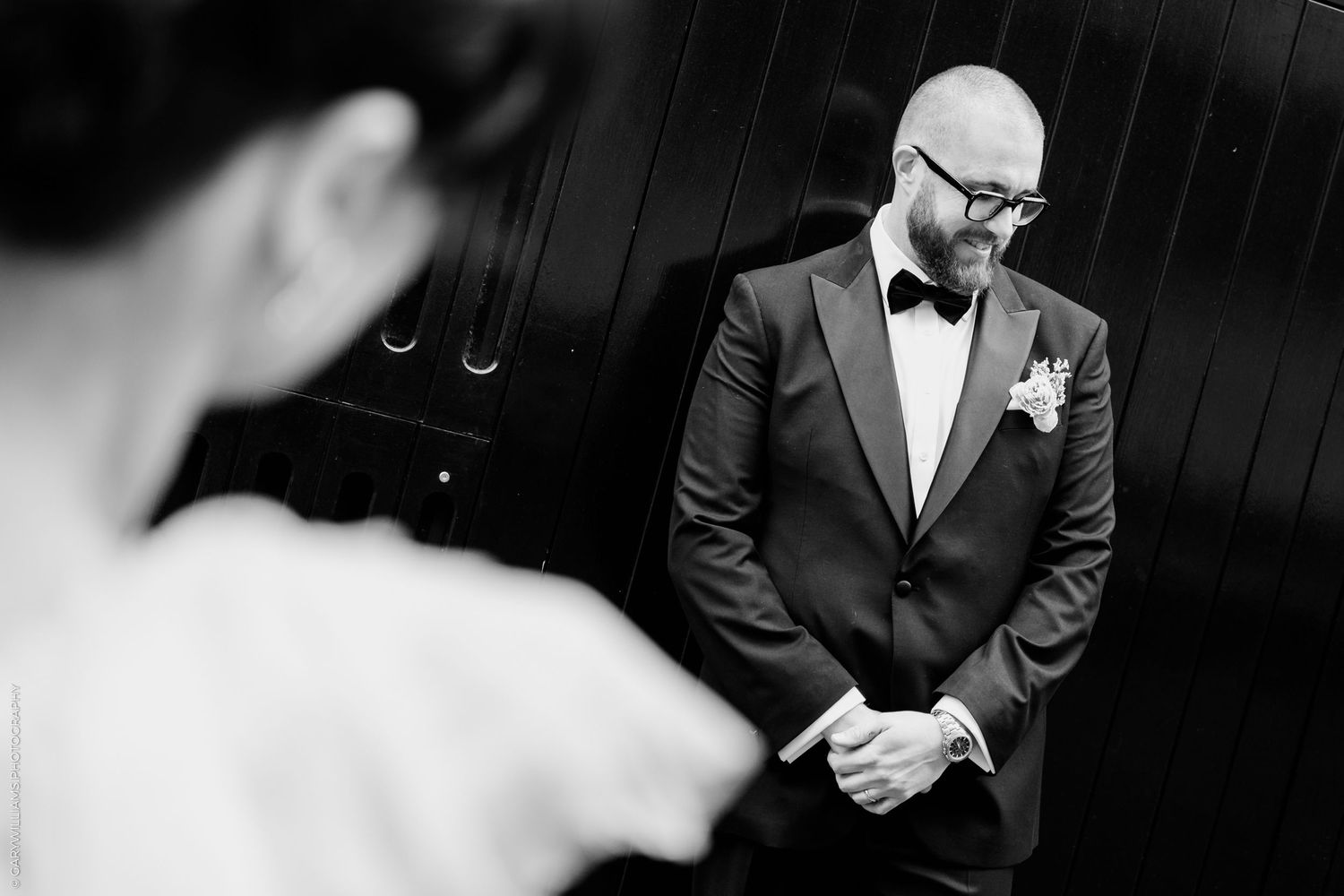 Black and white photo of an emotional groom in a tuxedo seeing his bride for the first time on their wedding day.