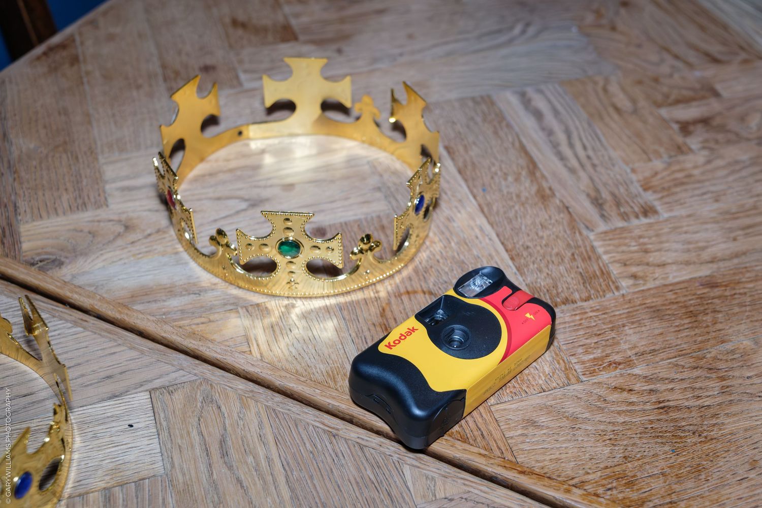 Gold royal crown and Kodak disposable camera on a wooden parquet floor.