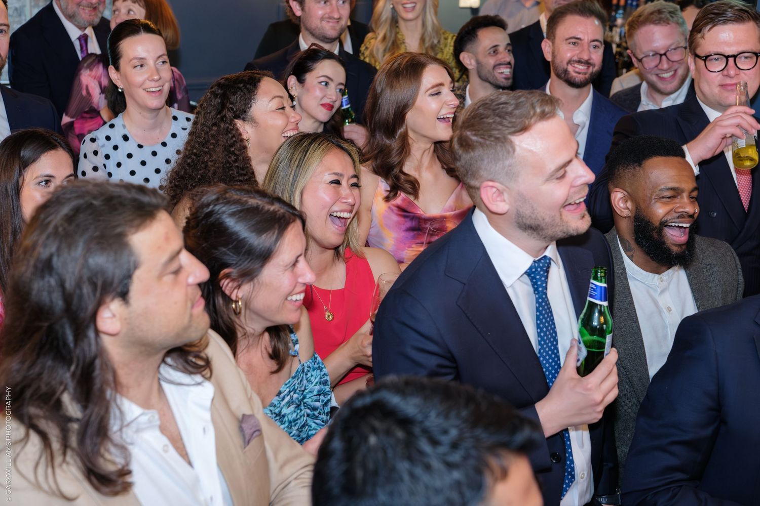 A diverse group of smiling professionals laughing together at a corporate networking event or party.