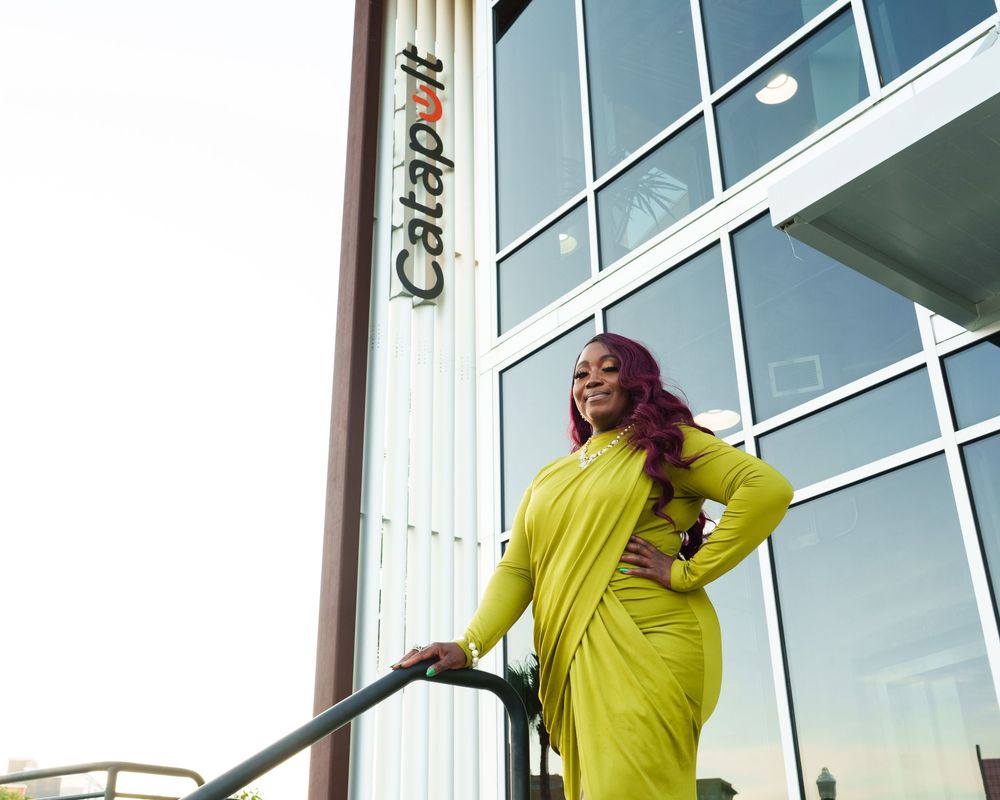 Woman in yellow dress posing confidently outside Catapult building with modern glass facade.