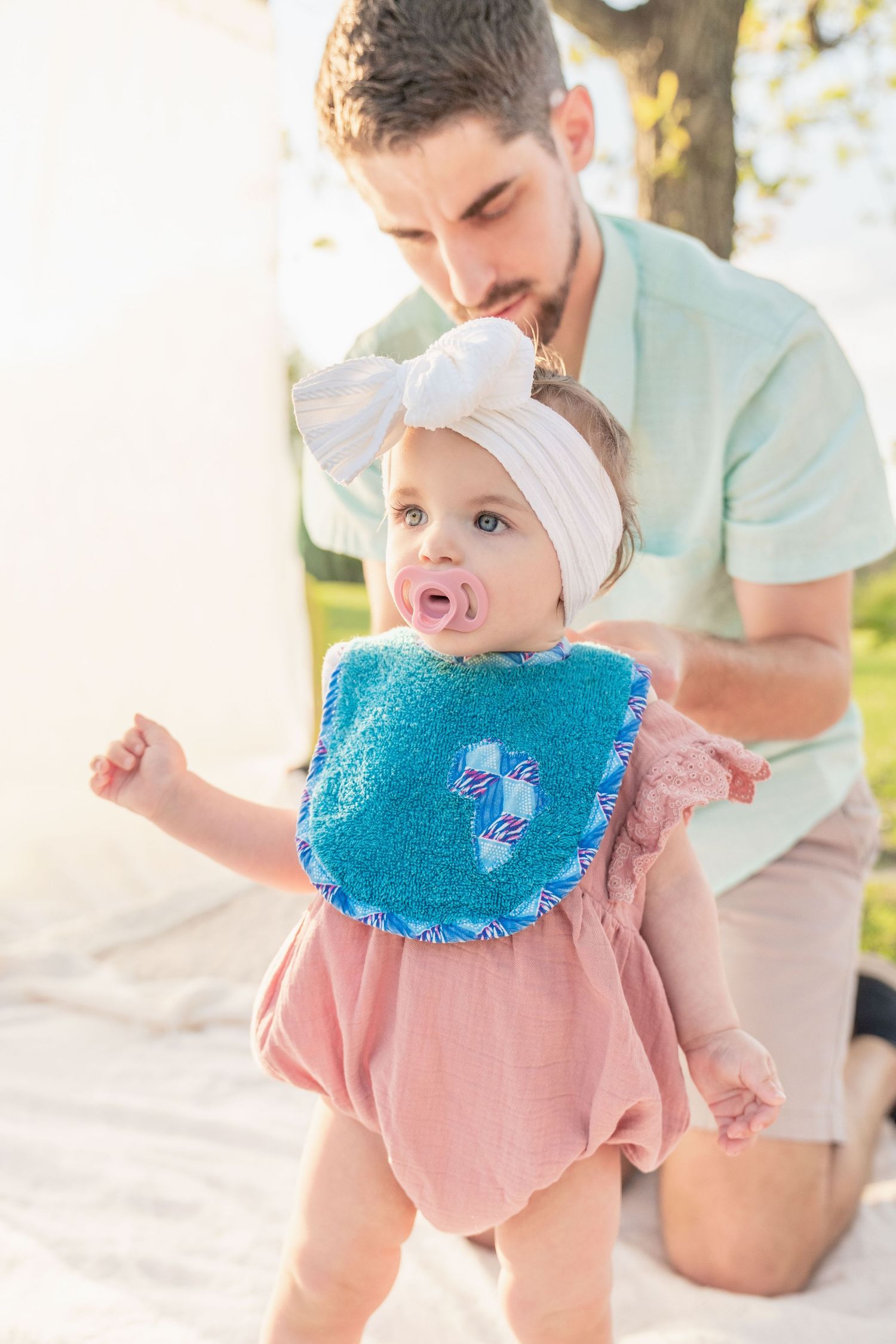 toddler girl cake smash one 1 year milestone outdoor photography, dad putting on blue bib on toddler