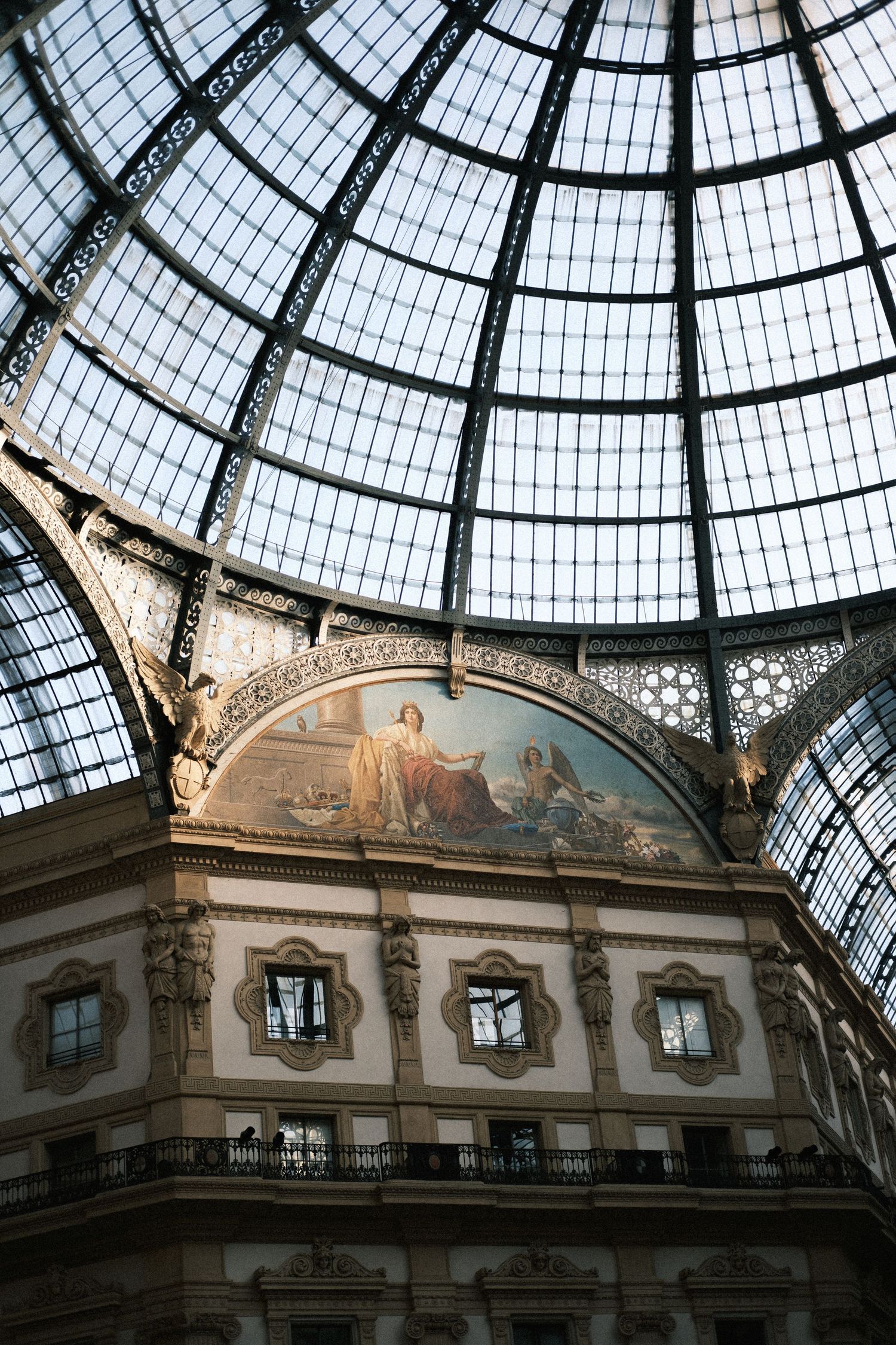 Ornate glass dome ceiling of Galleria Vittorio Emanuele II in Milan, Italy, with classical fresco and elegant architecture.