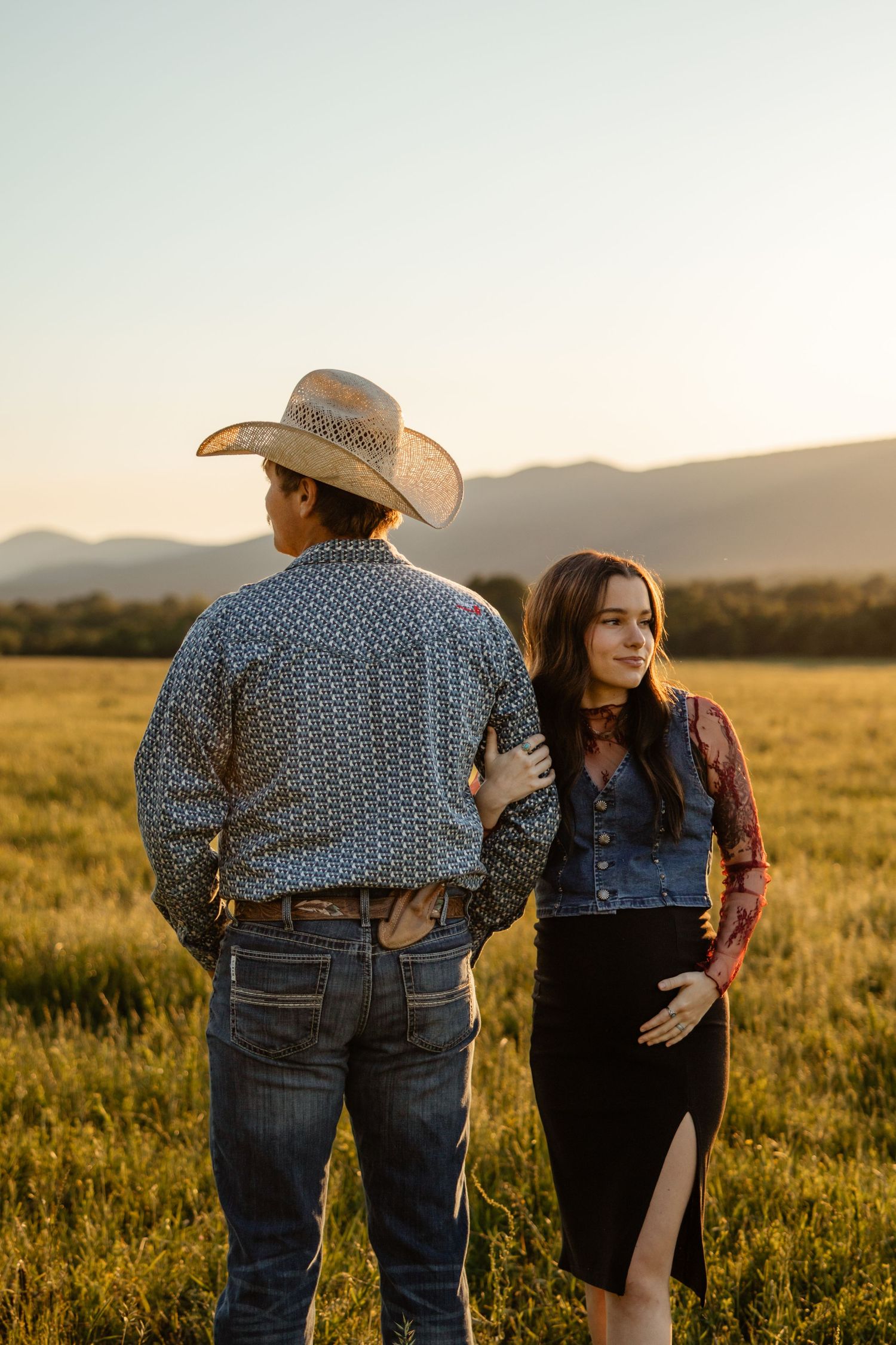 Couple sits together in field with mountain backdrop during intimate photo session.