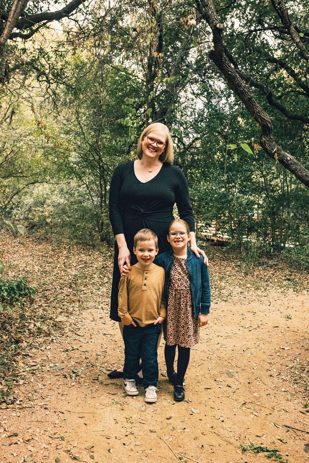 A family enjoying a walk together on a dirt trail surrounded by lush green trees on an autumn day.
