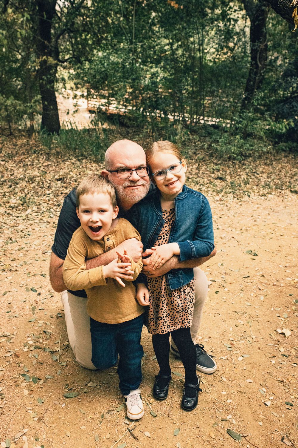 A playful moment captured on a dirt trail as three people huddle together and smile beneath the trees.