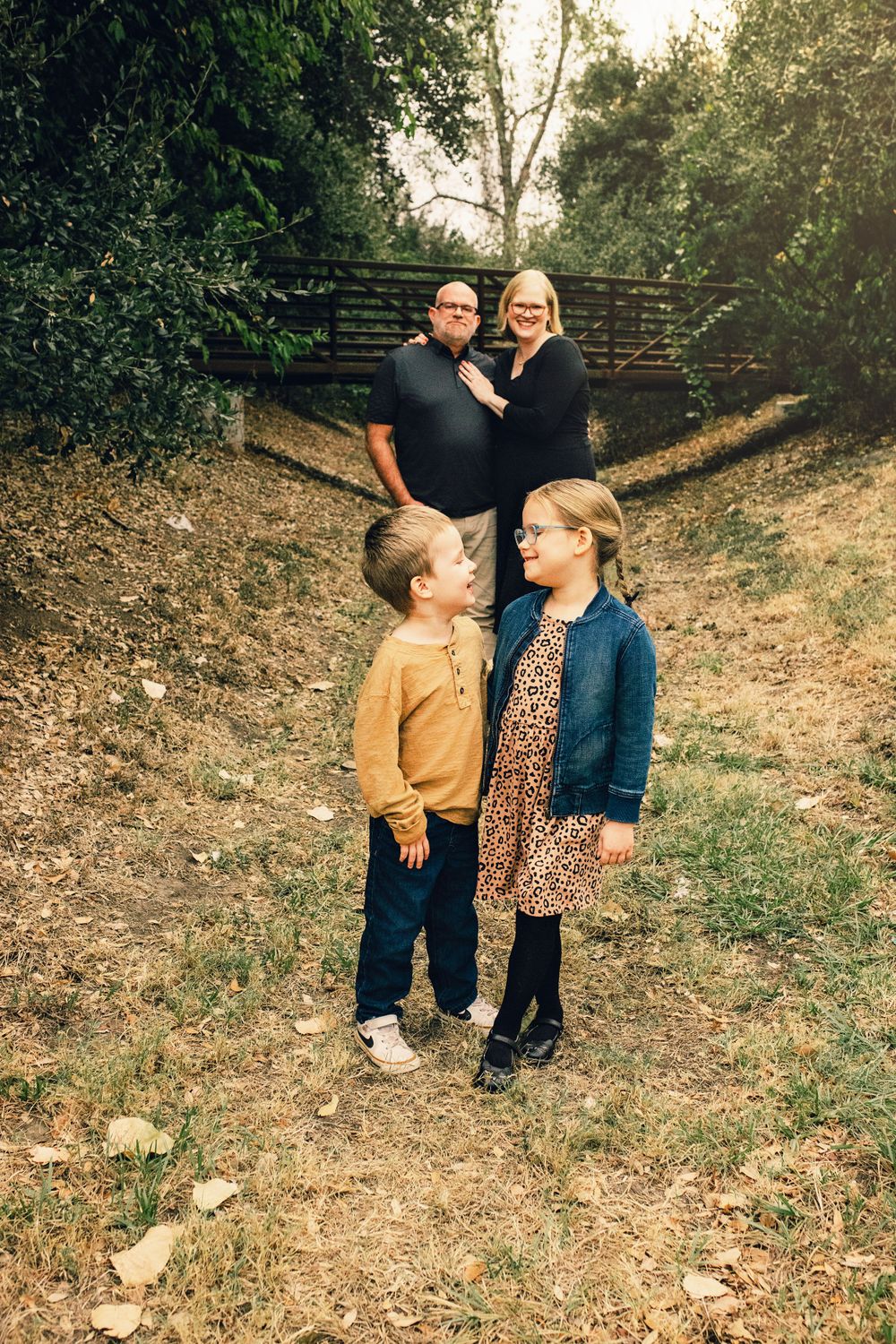 Family poses together on autumn trail surrounded by trees with golden sunlight filtering through branches.