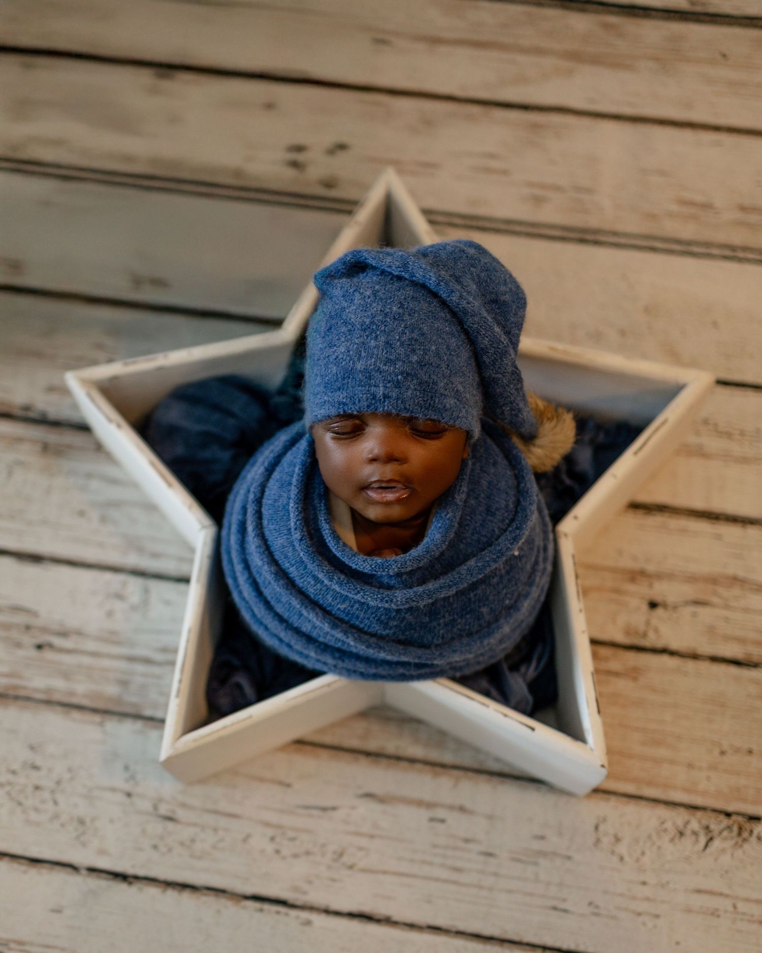 A person wearing a cozy blue winter beanie and scarf is photographed from above in a decorative star-shaped wooden frame.