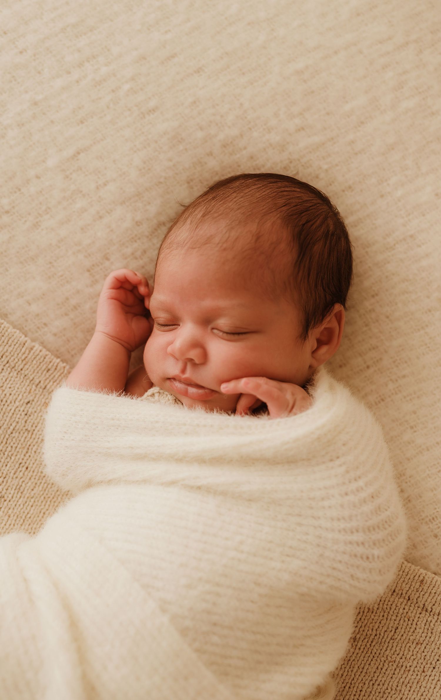 Peaceful sleeping newborn wrapped in soft white blanket while being cradled in loving arms.