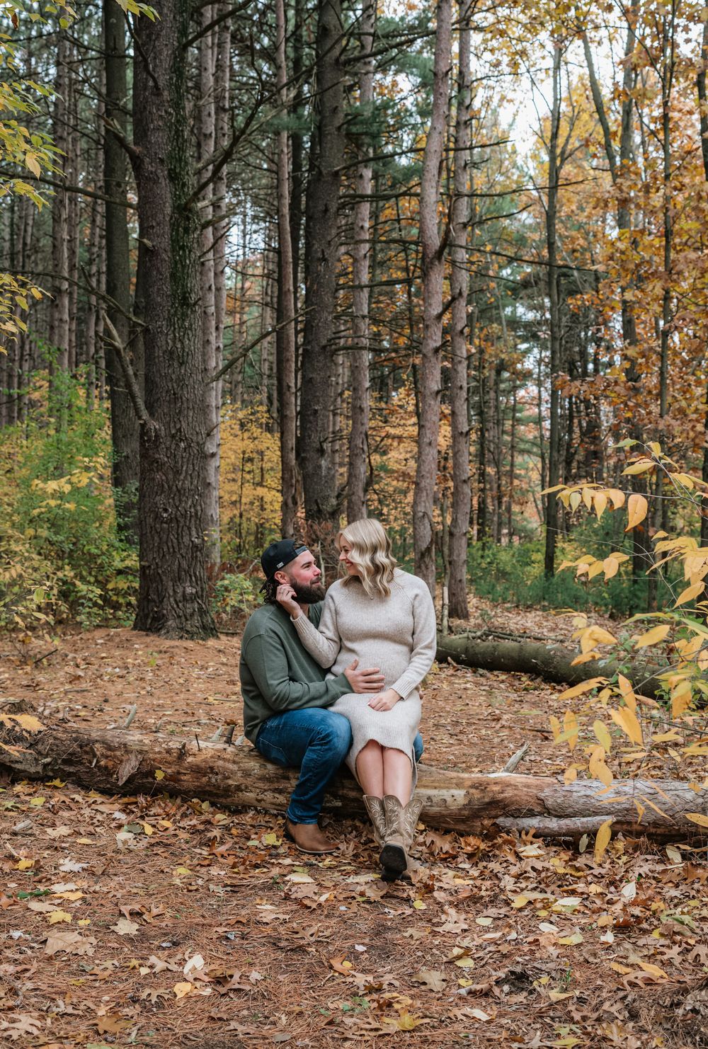 maternity couple sitting on log in woods