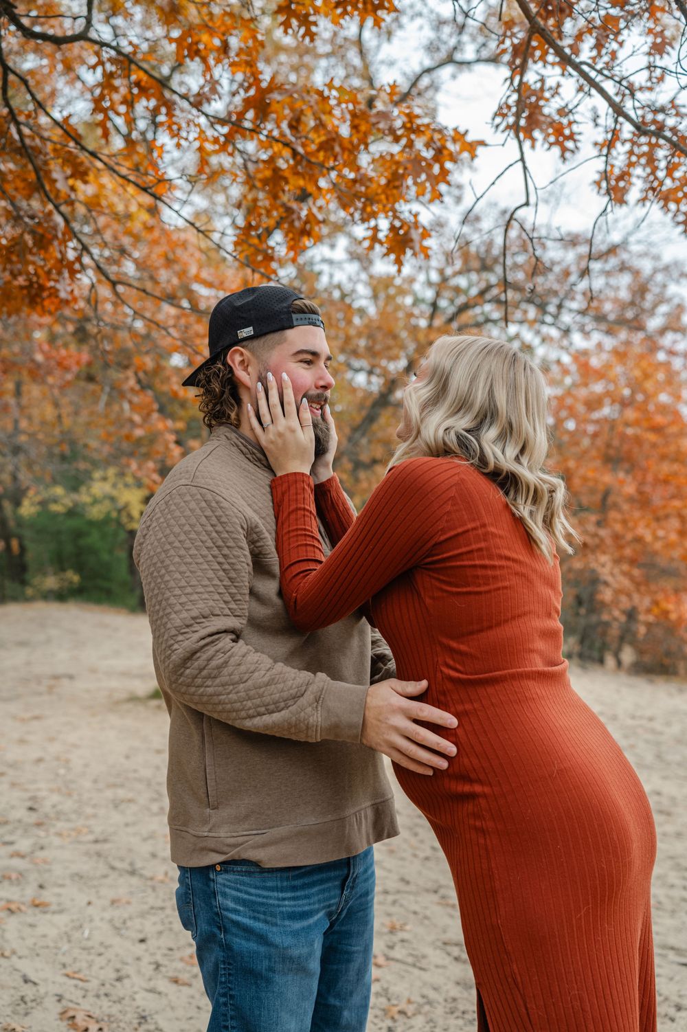 pregnant woman holding the face of her husband smiling at him as he hold her belly