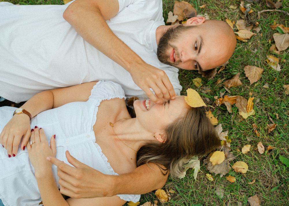 engaged couple laying on ground playing with leaves