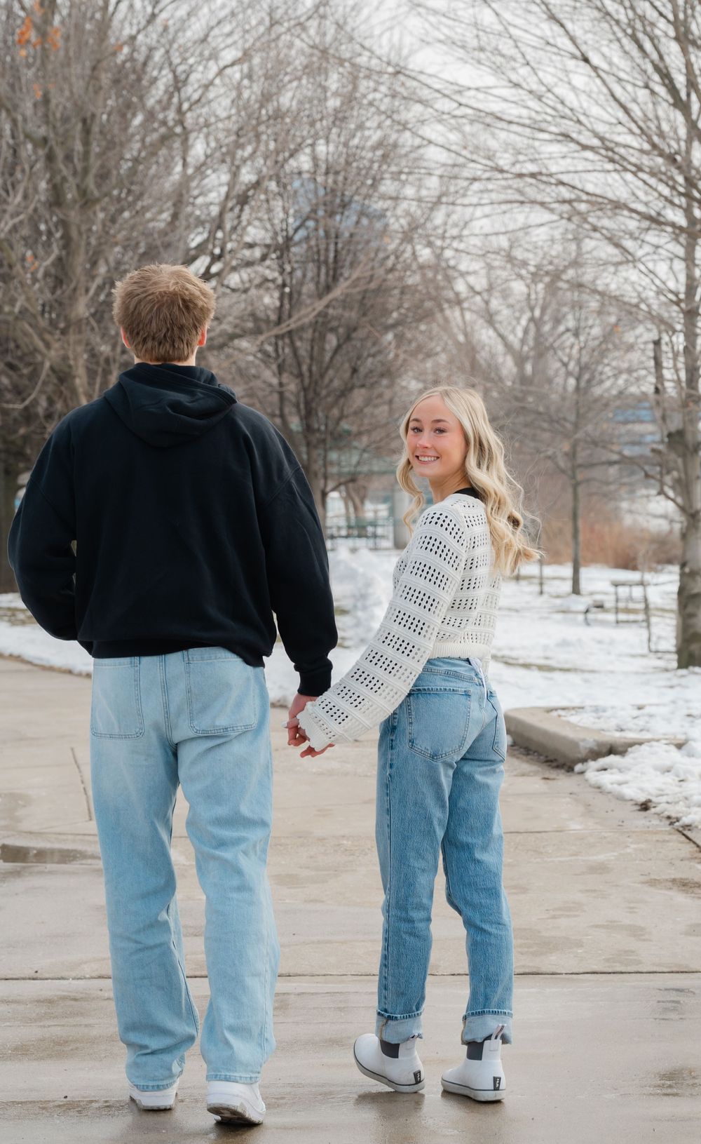 couple walking along grand river holding hands while girl looks back