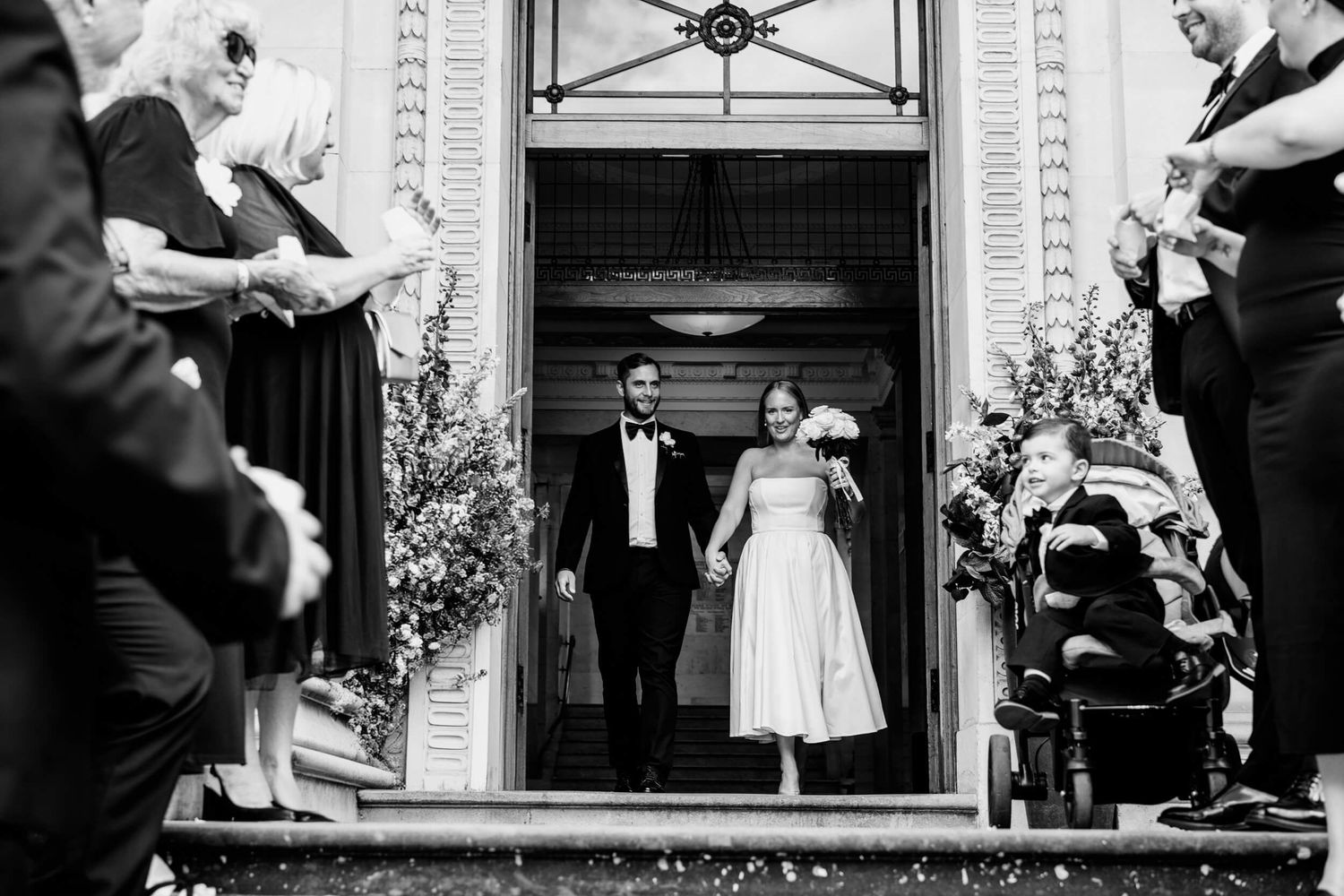 Black and white vintage wedding photo showing couple exiting church doors while guests throw rice in celebration.