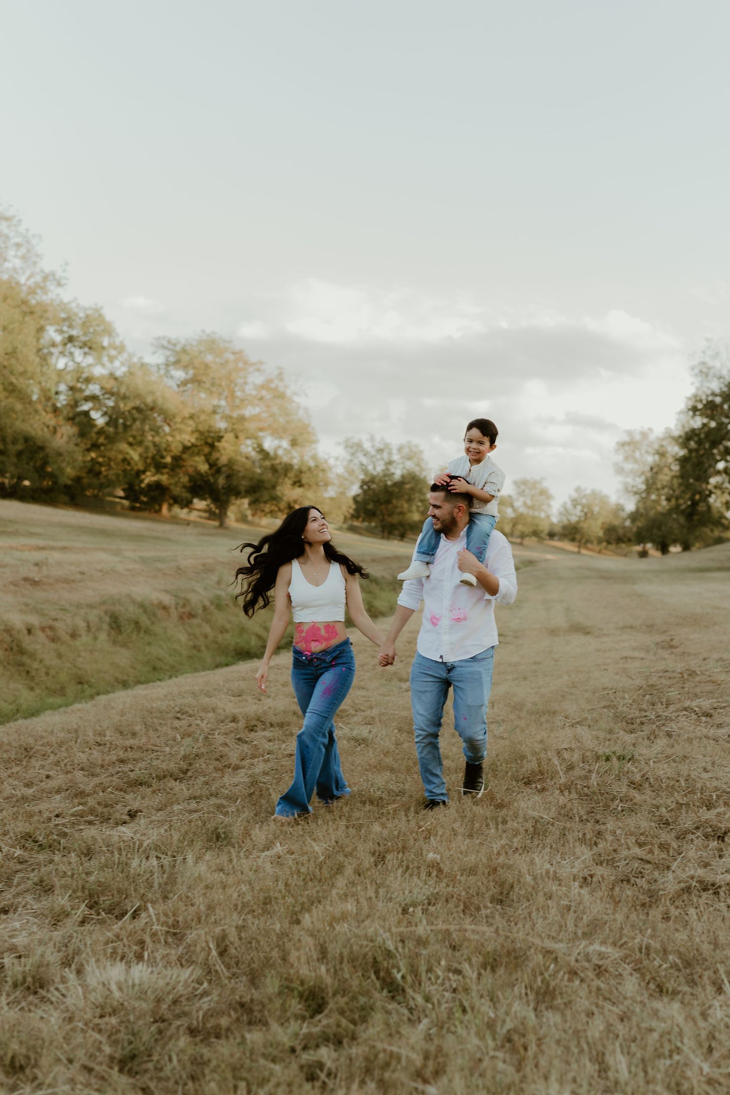 Couple runs playfully through a grassy hillside during sunset photo session.