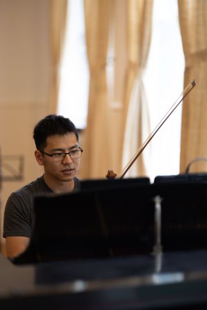 Musician sitting at music stand during rehearsal in warm-lit room.