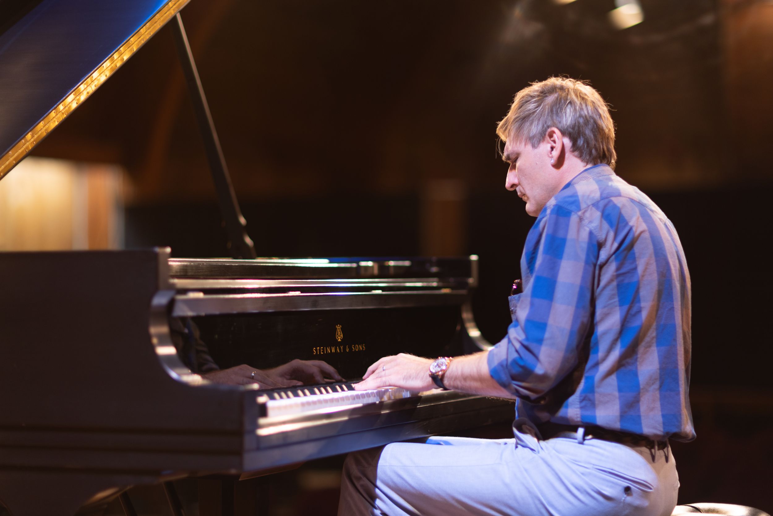 Pianist performing at grand piano on dimly lit concert stage.
