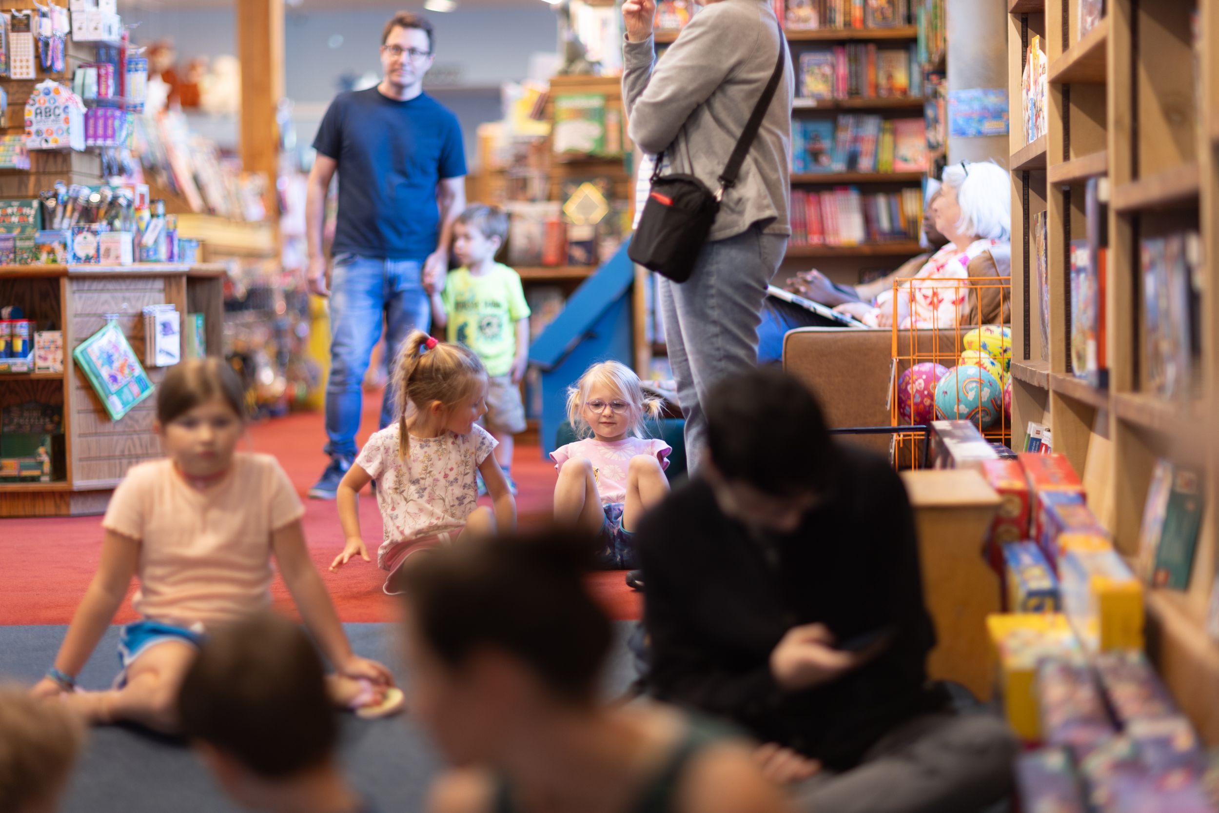 Performers and audience members gather in a bookstore setting with shelves of books visible.