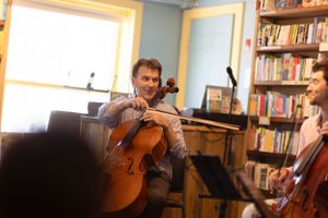 Musicians play string instruments in a library setting with bookshelves lining the walls.