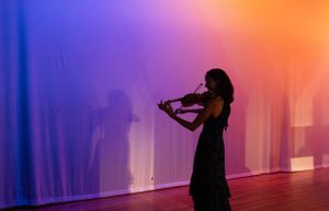 Silhouettes of performers against a colorful purple and orange backdrop.