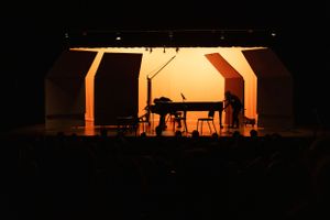 Backlit silhouettes of performers and instruments on a darkened stage.