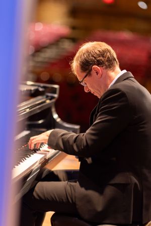 A pianist performs on a grand piano under dramatic stage lighting.