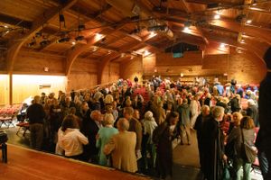A large crowd gathers in a rustic wooden venue space with warm lighting and exposed beams.