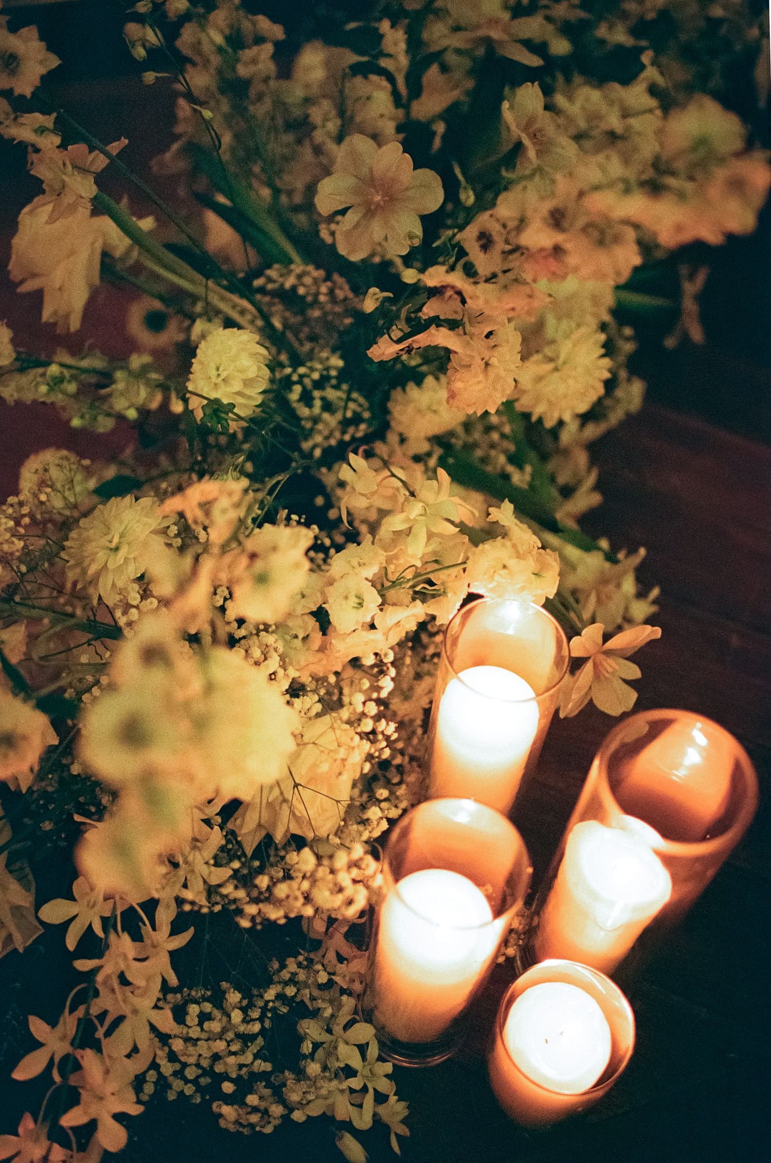 A romantic arrangement of glowing candles next to delicate white flowers and baby's breath in warm evening lighting.