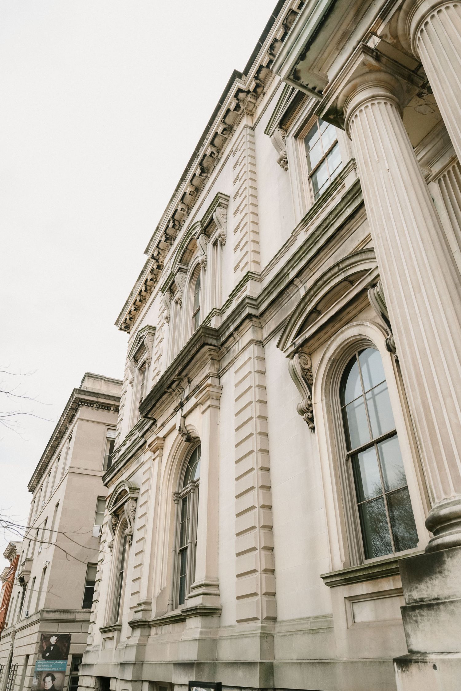 Low-angle architectural view of a neoclassical building with ornate white columns and tall arched windows.