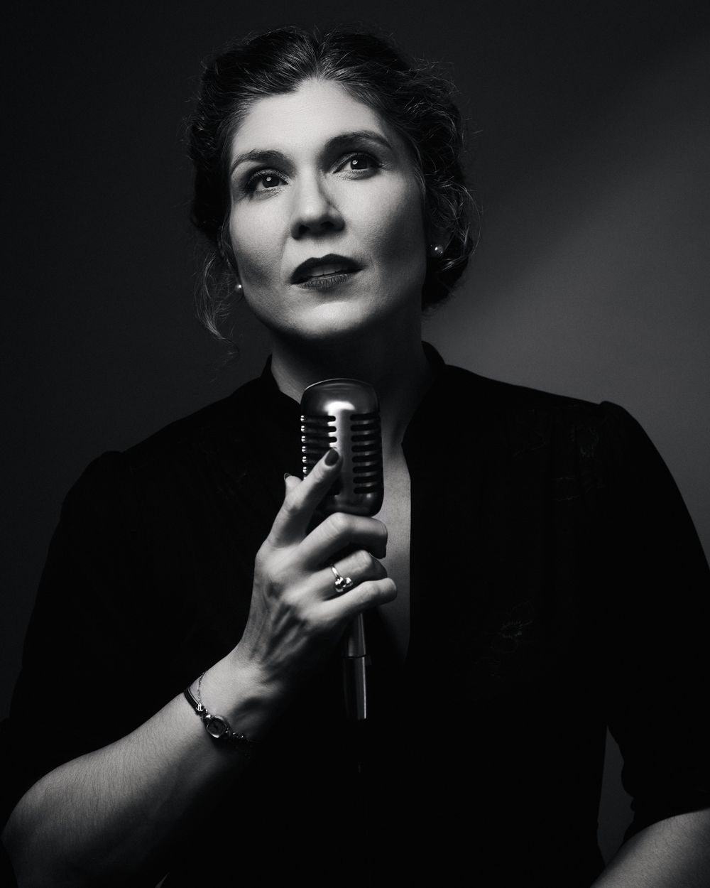Portrait of a woman with vintage curls and dark dress, lit in high-contrast noir tones with a velvet stillness.