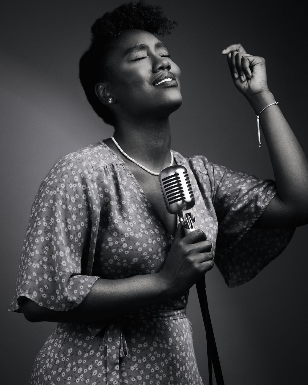 Emotive moment mid-song, eyes closed, hand lifted; soft loop lighting sculpts face and floral dress with vintage flair.