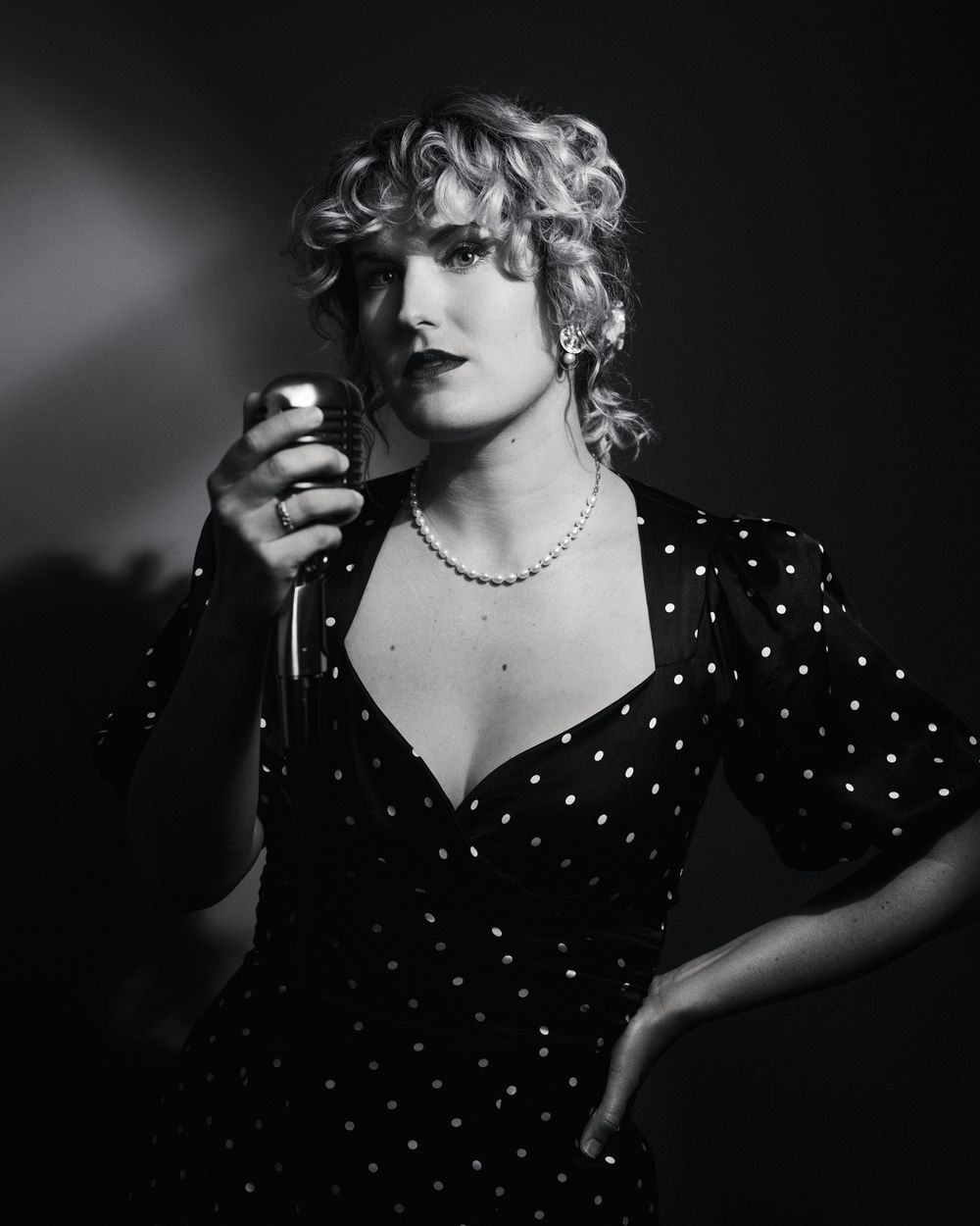 Jazz-age glam meets modern edge: woman in polka dots holding a retro mic, framed in cinematic shadows.