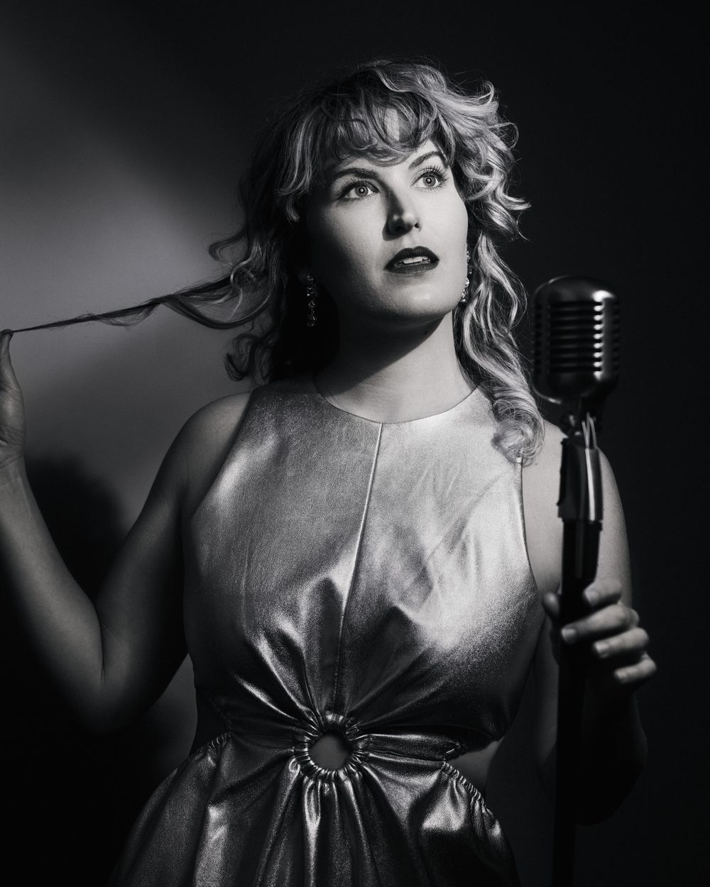 Woman in metallic gown twirling her hair, looking like a lost frame from a jazz film — PML with a wink.