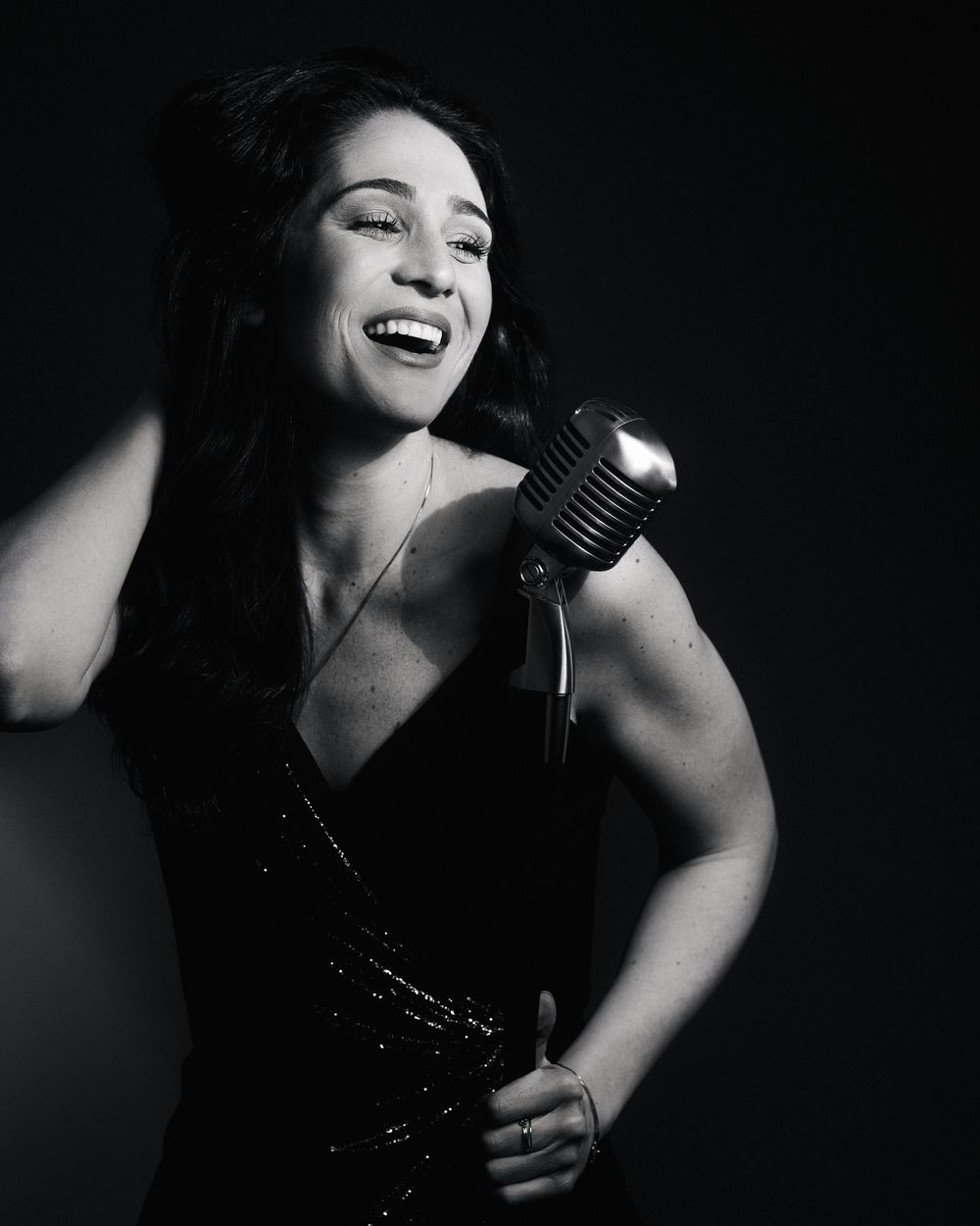 Woman in sequins laughing mid-phrase, vintage mic in hand — pure joy under 1940s-inspired light.