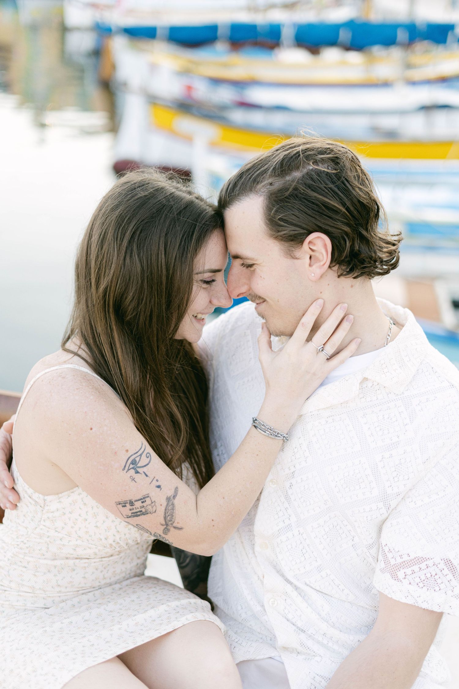 Intimate romantic moment between couple in white clothing with boats in background at marina.