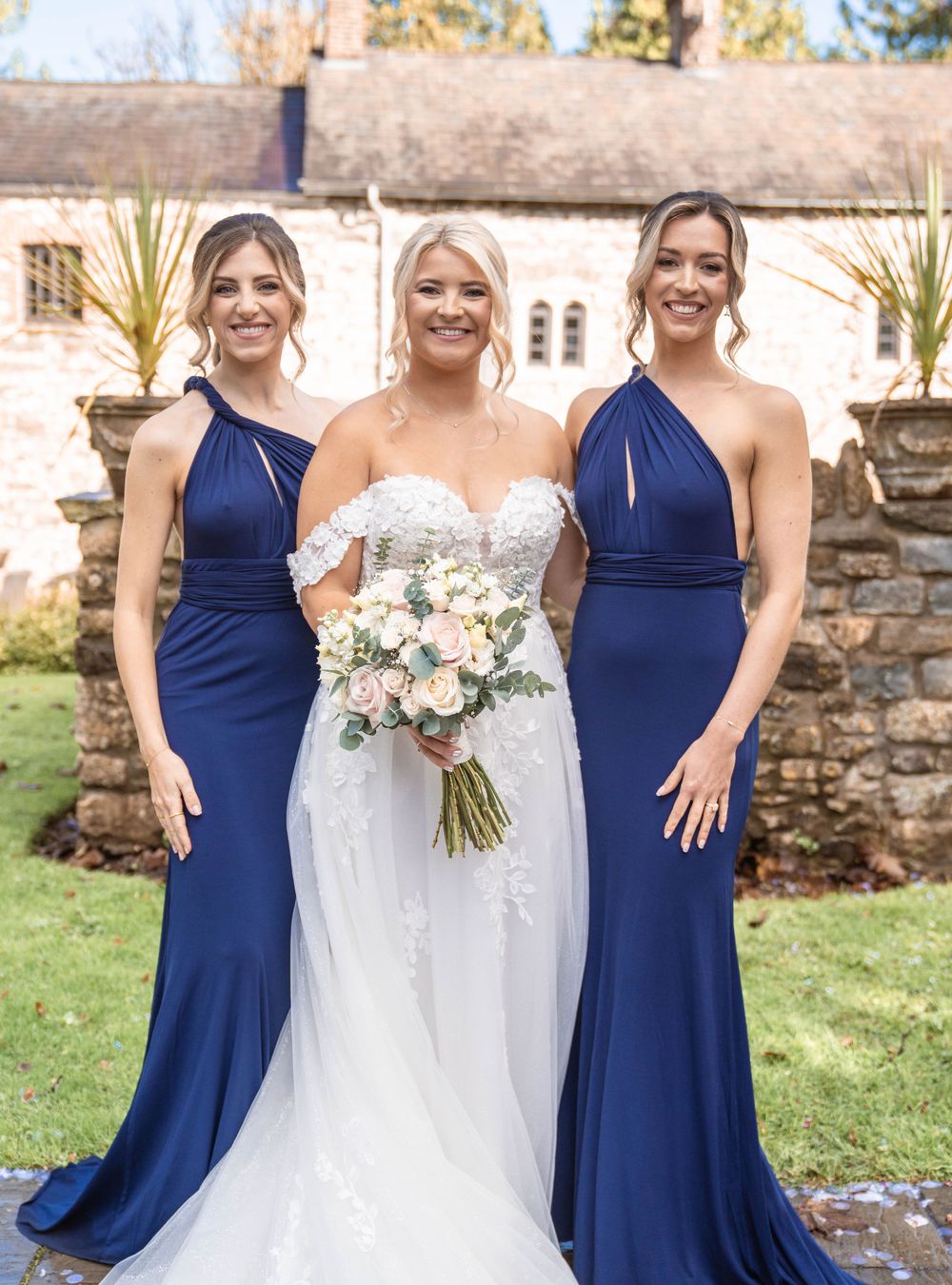 Wedding party with bridesmaids in navy dresses and bride in lace gown outdoors.
