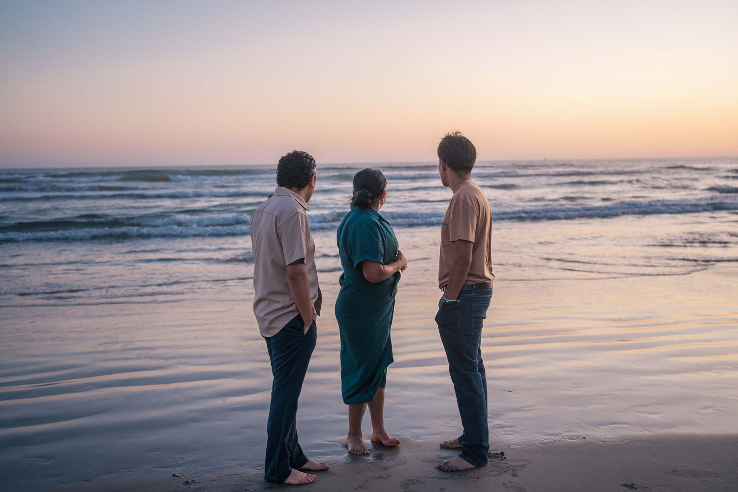 A group stands together watching the ocean waves during sunset at the beach.