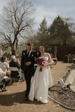 An outdoor wedding ceremony with white chairs and natural landscaping.