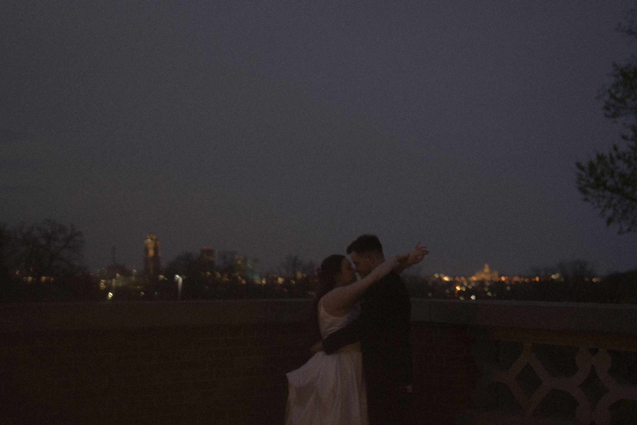 A silhouetted couple embraces against a city skyline at dusk.